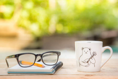glasses, pencil, notebook, white mug on the wooden table outdoor and copy space.の写真素材