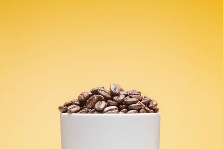 Coffee beans in white cup isolated on yellow backgroundの写真素材