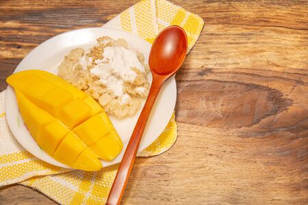 Thai mango and sticky rice with coconut milk desserts on white dish with wooden background. Mango is Thailand's tropical fruit. Top viewの写真素材