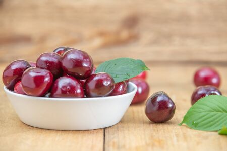 Fresh cherries in the white bowl on wood tableの写真素材