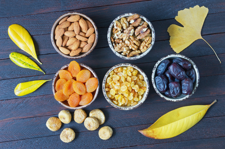 Autumn. Various nuts and dried fruits (walnuts, almonds,  dried apricots, raisins, date fruits, figs ) and yellow leaves on dark wooden table. Flat layの写真素材