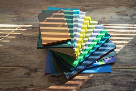 Stack of books of different sizes and colors on table lit by streaks of light from window