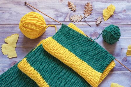 Knitting on autumn day. Warm striped yellow-green scarf with knitting needles and balls of wool on rustic backgroundの写真素材