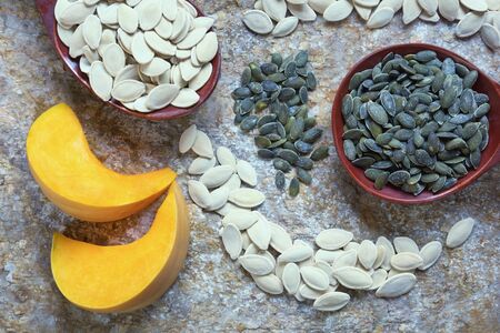Pumpkin slices and seeds - in shell and peeled. Two large wooden spoons with pumpkin seeds. Natural stone backgroundの写真素材