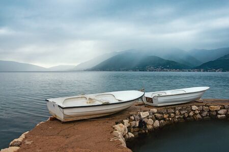 Rainy day. Two white fishing boats on the shore. Montenegro, Adriatic Sea, view of Bay of Kotor near  Tivat cityの写真素材