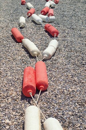 Preparing to summer beach vacation,  concept. Sunny pebble beach with string of red and white buoysの写真素材