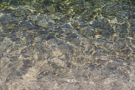 Abstract natural colorful background. Shallow water on a pebble sea beach on a calm sunny dayの写真素材