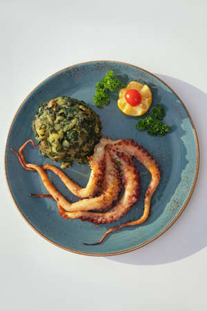 Balkan cuisine. Plate with grilled octopus and green leafy vegetables on white table. Flat lay, copy spaceの写真素材