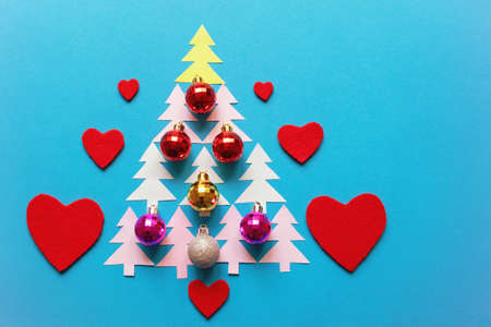 Bright colorful Christmas balls and red felt hearts. Paper fir-trees in the form of a Christmas tree. Flat lay, free space for textの写真素材