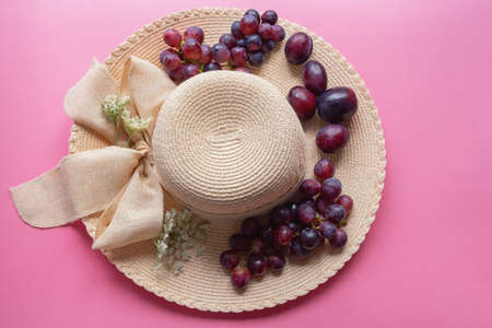 Summer concept. Grapes, plums and flowers on brim of sun hat. Free space for textの写真素材