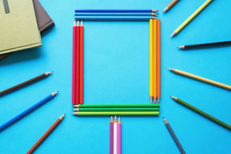 Colorful colored pencils and books on blue paper background. Flat lay, frame with free space for textの写真素材
