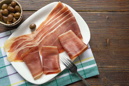 Balkan cuisine . Slices of prsut: dry-cured ham,  prosciutto. Dark rustic table. Copy spaceの写真素材