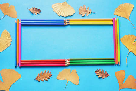 Autumn and school concepts. Frame for text from bright colored pencils. Yellow leaves, blue paper background. Flat layの写真素材