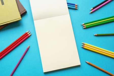 School concept. Colorful colored pencils, books and open sketchbook on blue paper background. Flat lay, free space for text or pictureの写真素材