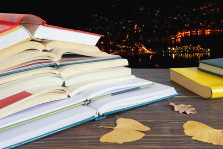 Open books and yellow leaves on the table against of night town backgroundの写真素材