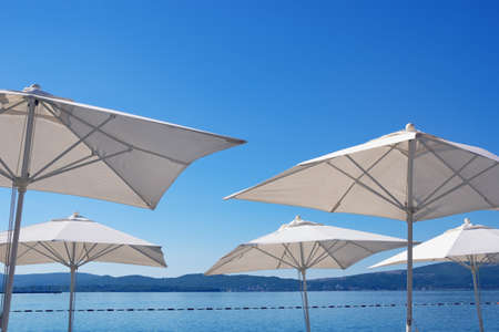 Beach vacation concept. White sun umbrellas on blue sky background. Montenegro,  view of Kotor Bay near Tivat city. Free space for textの写真素材