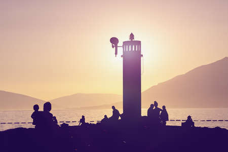Beach vacation concept. Mediterranean landscape with silhouettes of lighthouse and tourists at sunset. Montenegro,  Bay of Kotor, Tivatの写真素材