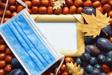 Autumn concept. Fresh fruits (Jujube fruits, plums; grapes ), yellow autumn leaves and face protective mask. Copy spaceの写真素材
