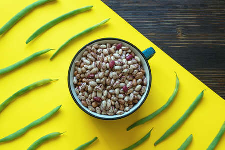 Beans in pot and fresh green beans on yellow paper background. Free space for textの写真素材