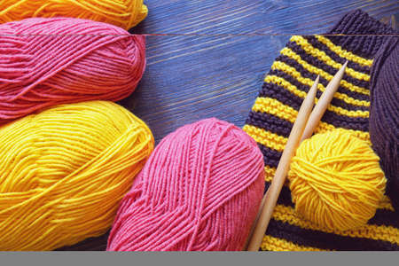 Hobby concept, knitting. Colorful clews of wool on dark rustic table. Unfinished striped knitting, knitting needles. Copy spaceの写真素材