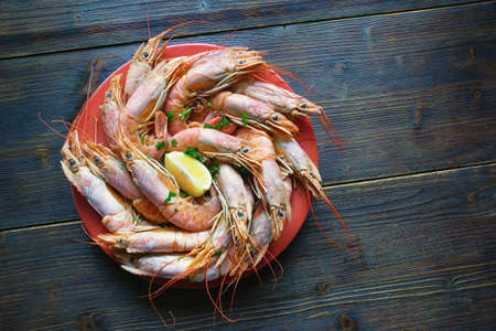 Dish with boiled pink shrimps and slice of lemon on dark rustic table. Copy spaceの写真素材