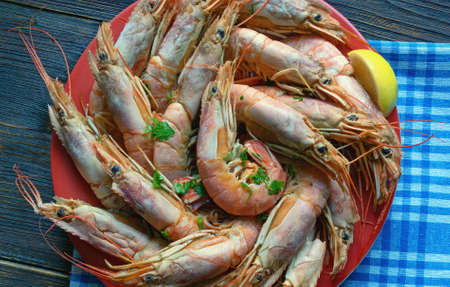 Boiled pink shrimps in red plate on rustic table. Flat layの写真素材