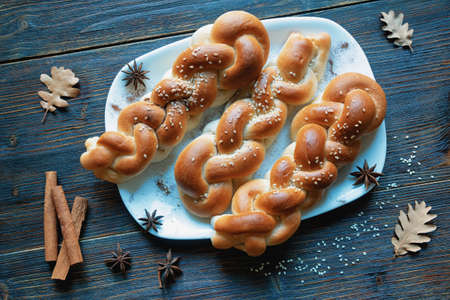 Homemade  sweet braided pastries with cinnamon,  sesame seeds  and star anise seeds on  dark rustic table. Autumn oak leaves. Copy spaceの写真素材