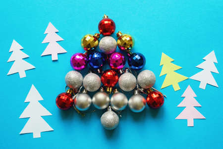 Bright colorful Christmas balls in the form of a Christmas tree and paper fir-trees on blue background. Flat lay, free space for textの写真素材