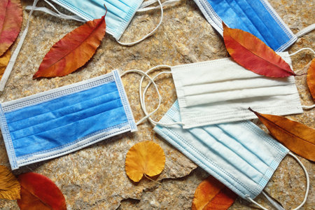Old discarded medical face masks among colorful autumn leaves. Environmental pollution problemの写真素材