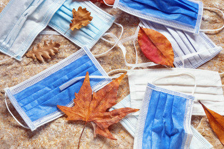 Old discarded medical face masks among autumn leaves. Environmental pollution problemの写真素材