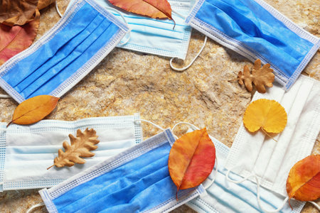 Old discarded medical protective face masks on stone among  autumn leaves. Environmental pollution conceptの写真素材