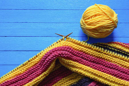 Hobbies concept.  Bright striped knitted cloth with knitting needles and ball of wool on  blue rustic table. Copy spaceの写真素材