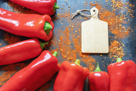 Bright red bell peppers and cutting board with crushed hot paprika scattered on black metal background. Flat lay, space for textの写真素材