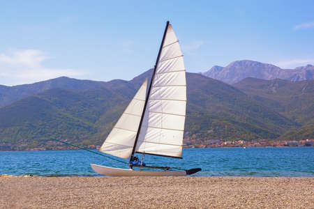 Sailboat with white sail on beach. Vacations and recreation concept. Montenegro, Adriatic Sea, Bay of Kotorの写真素材