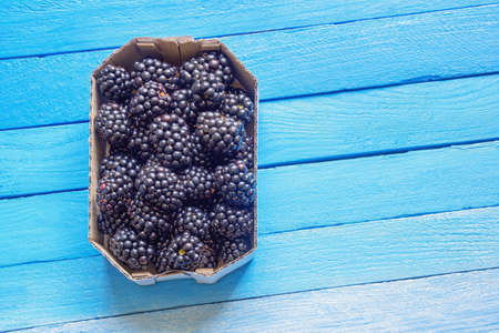 Blackberries from market.  Fresh ripe blackberries in cardboard box on blue rustic table. Flat lay. Free space for textの写真素材