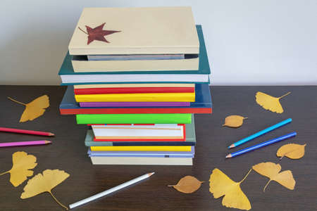 School concept. Stack of  different books, autumn leaves and colored pencils on tableの写真素材