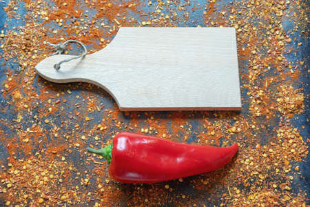 Bright red bell pepper and cutting board with crushed hot paprika scattered on black metal background. Space for textの写真素材