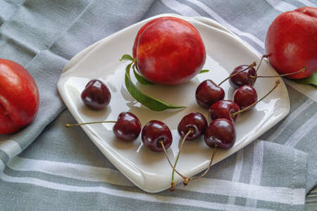 Red fruits. Fresh ripe cherries and nectarines on white plateの写真素材