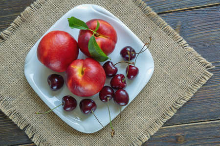 Fresh ripe cherries and nectarines on white plate. Rustic table. Flat layの写真素材