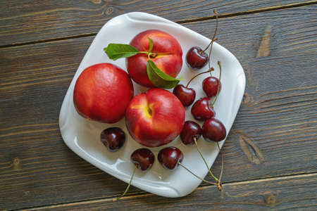 Fresh ripe fruits - cherries and nectarines - on white plate. Rustic background. Flat lay, copy spaceの写真素材