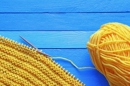 Hobbies and knitting concept.  Yellow knitted cloth with knitting needles on  blue rustic table. Copy spaceの写真素材