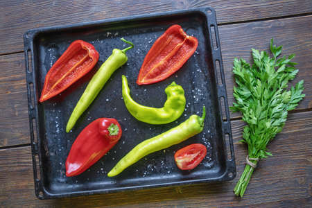 Bright vegetables on black  baking sheet.  Green and red peppers, tomatoes, bunch of parsley.   Flat layの写真素材