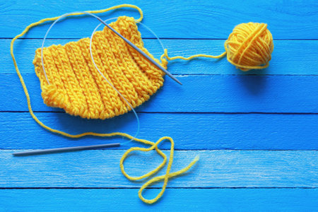knitting, hobbies concept.  Yellow knitted cloth with knitting needles and ball of wool  on  blue rustic table. Copy spaceの写真素材