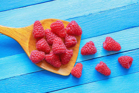 Red-fruited raspberries. Fresh ripe raspberries in wooden spoon on blue rustic table. Free space for textの写真素材