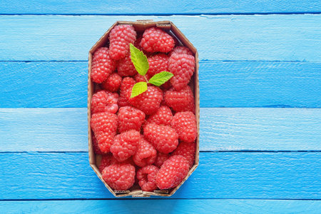 Red-fruited raspberries from market.  Fresh ripe raspberries in cardboard box on blue rustic table. Flat lay. Copy spaceの写真素材