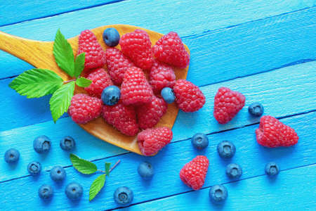 Fresh ripe berries in wooden spoon on blue rustic table. Raspberries and blueberries .  Free space for textの写真素材