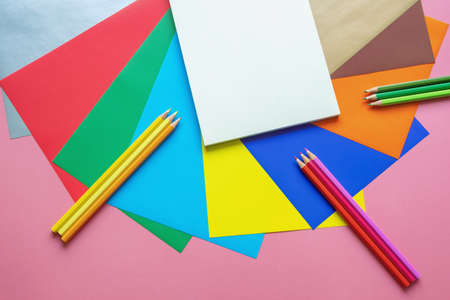 School and hobby concepts. Colorful colored paper sheets, colored pencils and open sketchbook on pink paper background. Free space for text or pictureの写真素材