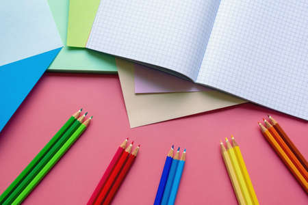 School and hobby concepts. Colored paper sheets, colored pencils and notebook on pink paper background. Free space for textの写真素材
