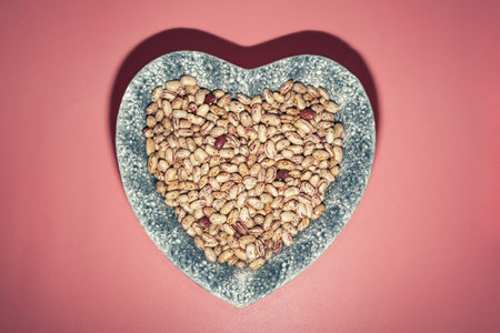 Brown haricot beans in heart-shape plate on pink table. Flat lay, copy spaceの写真素材