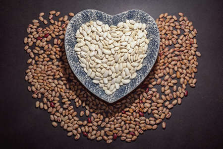 White haricot beans in heart-shape plate and brown haricot  beans on black tableの写真素材